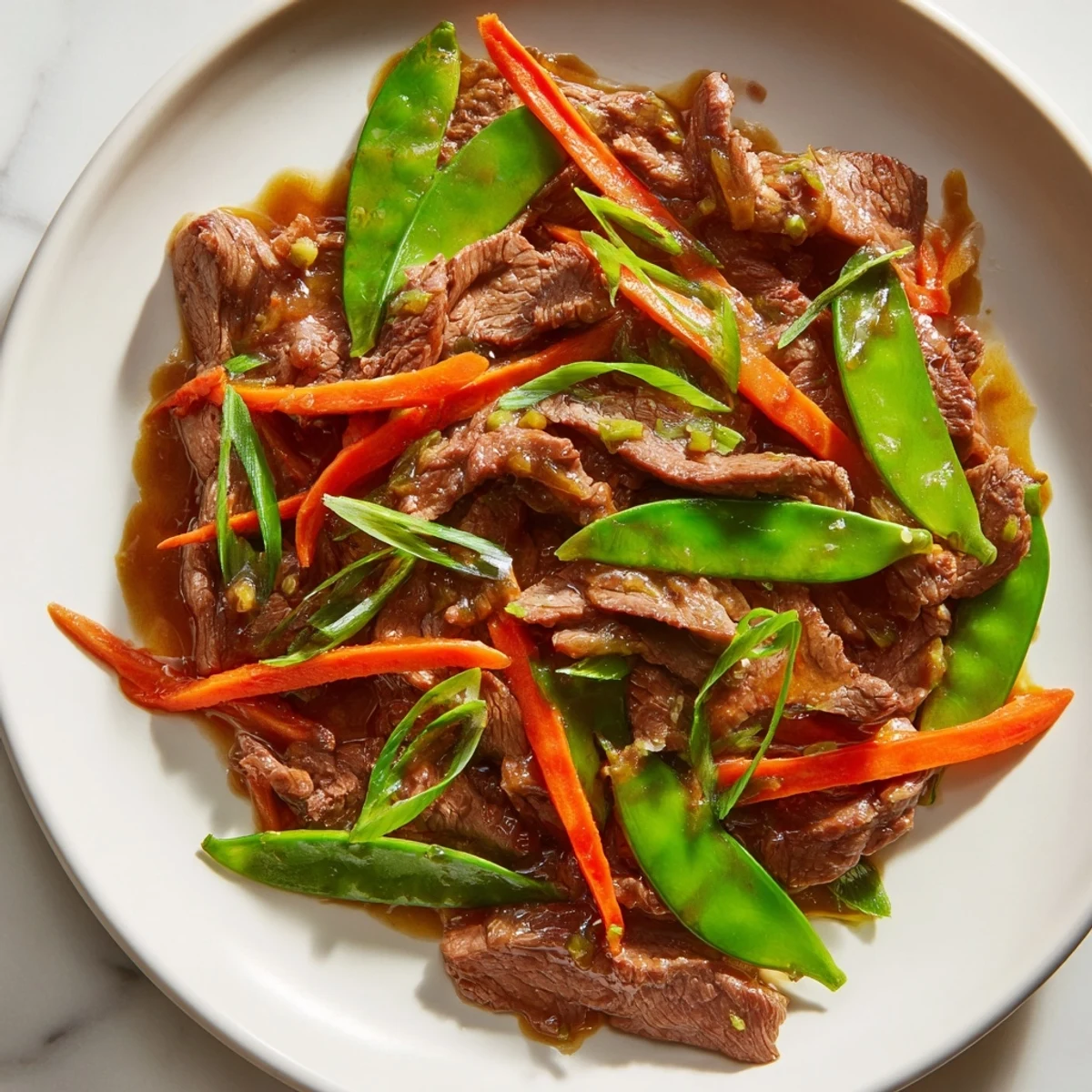 Tender slices of beef stir fry with snow peas and carrots, coated in a glistening, savory sauce, ready to serve.