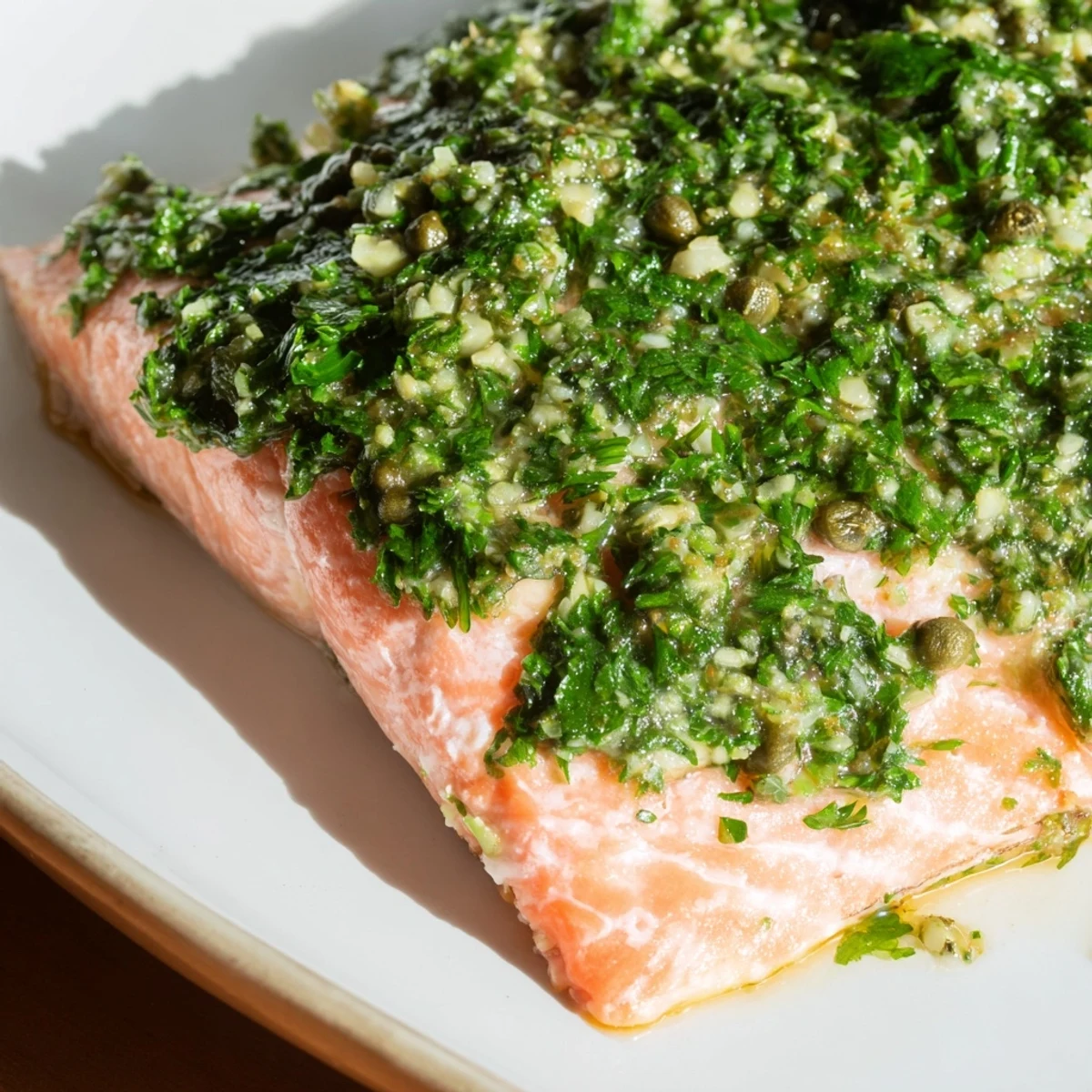 Golden-brown Baked Salmon with Salsa Verde resting on a white plate, garnished with fresh parsley and lemon wedges for a bright, zesty finish.