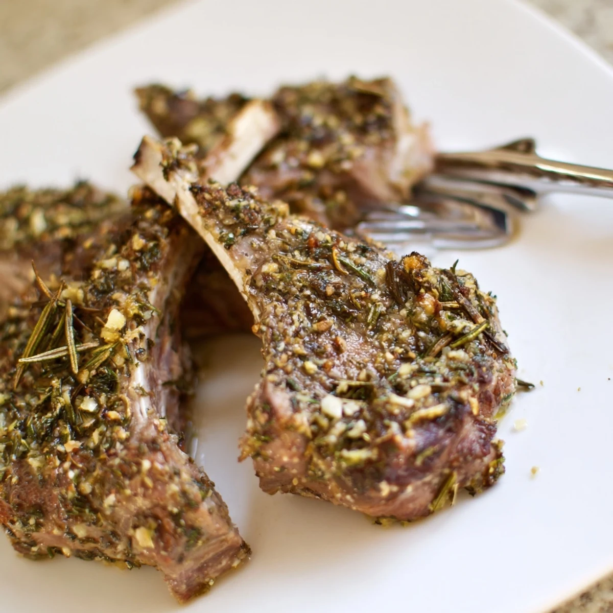 Juicy herb roasted lamb chops rest on a plate, garnished with fresh rosemary and lemon wedges.