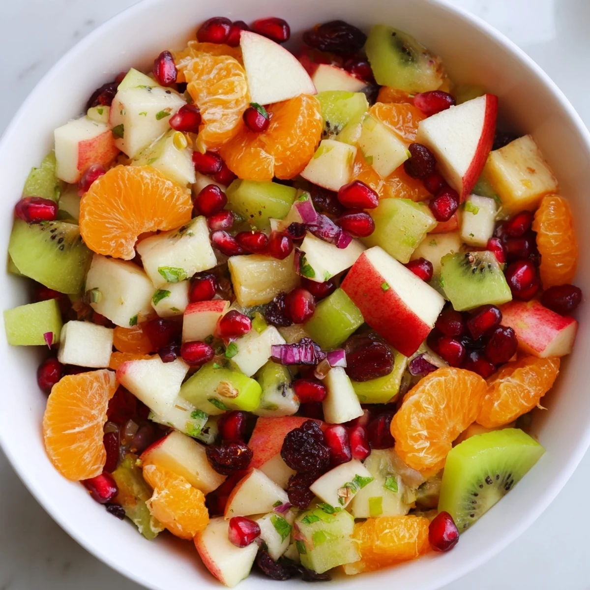 A large glass bowl of Winter Fruit Salad with Honey Lime Dressing, showcasing segmented oranges, diced apples, and glistening pomegranate arils.