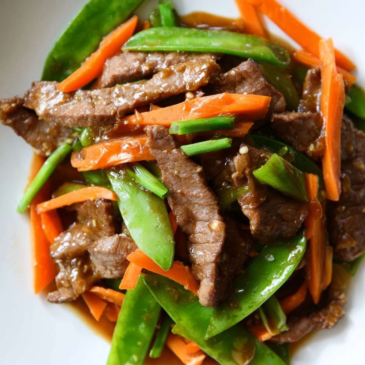 A close-up of Beef Stir Fry with Snow Peas and Carrots, featuring tender beef strips, crisp green snow peas, and vibrant orange carrots coated in a glossy, savory sauce.