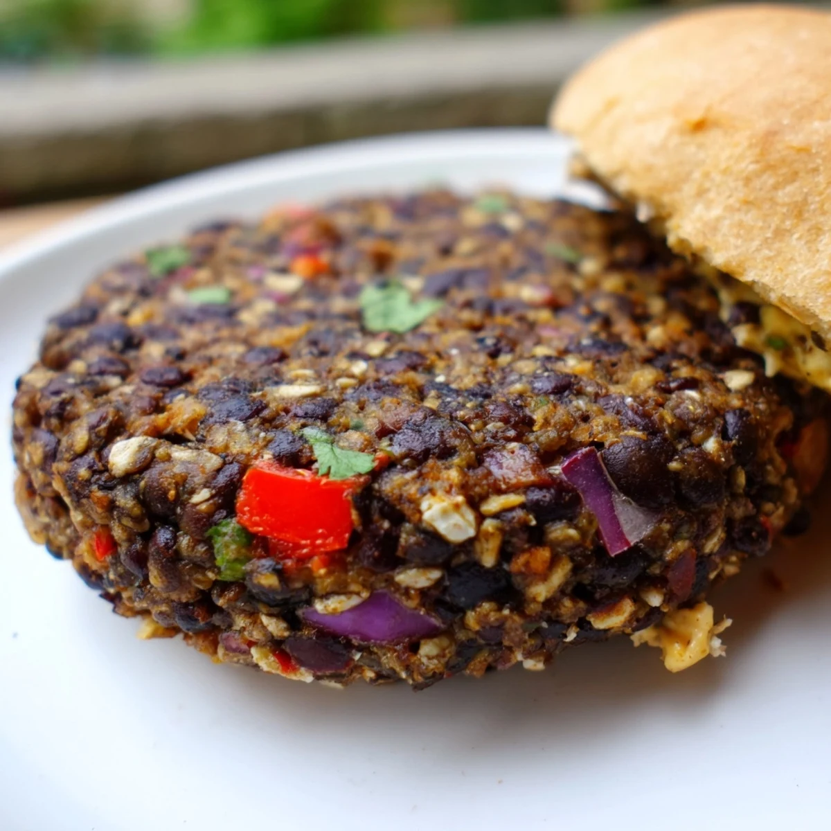 Stylized photo of a Vegan Black Bean Burger with Chipotle Lime Mayo served on a rustic plate with lime wedges and cilantro.