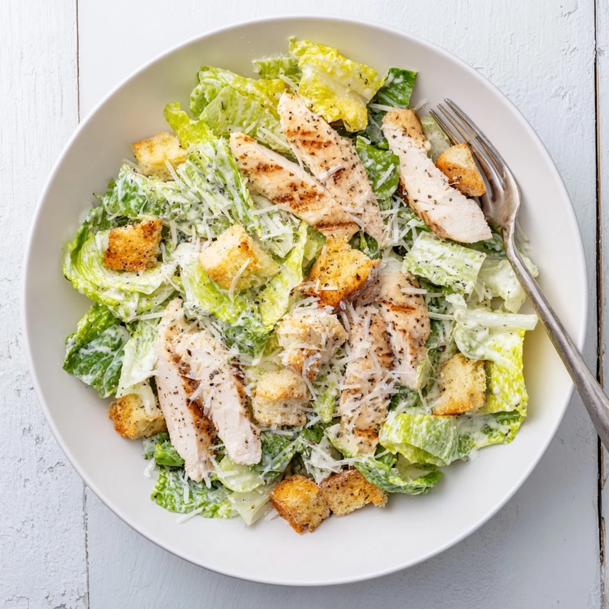 A close-up of vibrant Chicken Caesar Salad with crunchy homemade croutons, shaved Parmesan, and tender grilled chicken on a bed of greens.
