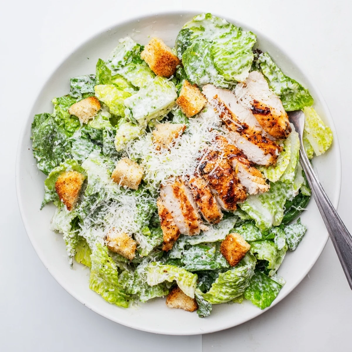 Freshly grilled chicken slices rest atop crisp romaine lettuce, creamy homemade Caesar dressing, and golden homemade croutons in this Chicken Caesar Salad.