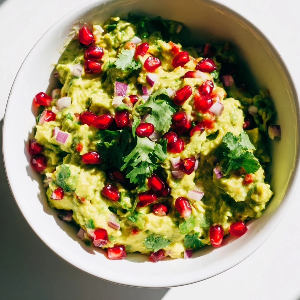 A close-up of Touchdown Spicy Guacamole in a rustic bowl, topped with fresh cilantro and pomegranate seeds.