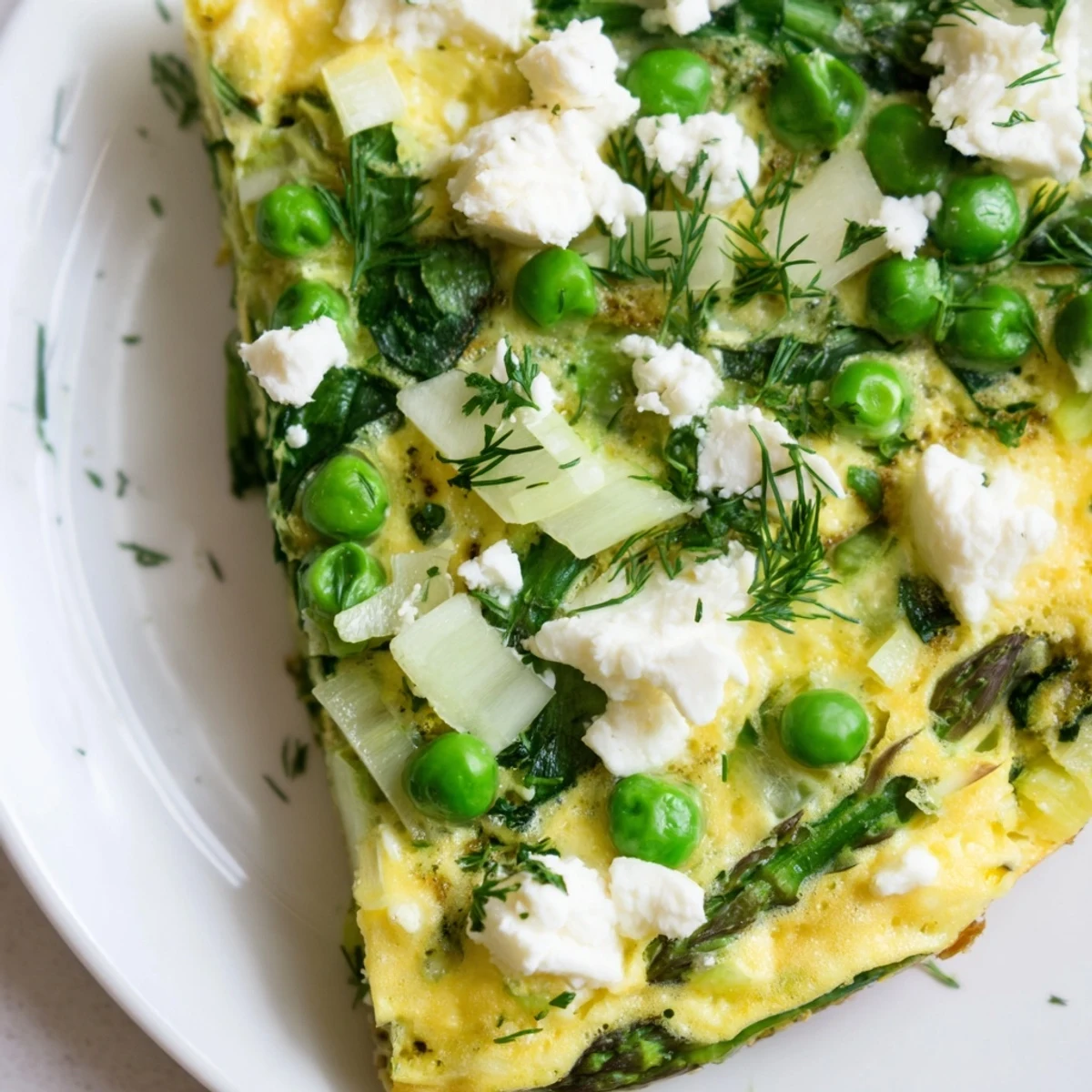 The finished Spring Vegetable Frittata with Goat Cheese and Herbs is sliced into wedges, showcasing fluffy eggs, tender asparagus, green peas, and melted goat cheese crumbles.  
