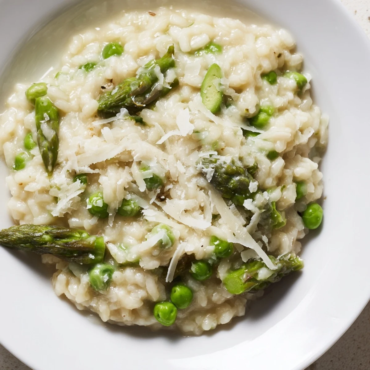 Spring-inspired creamy asparagus and pea risotto served warm with a lemon wedge on a wooden table.