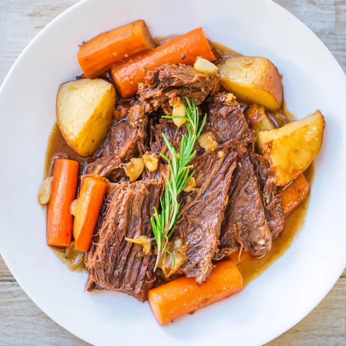 A rustic slow cooker pot roast with carrots beside carrots and sauce in a ceramic dish.  