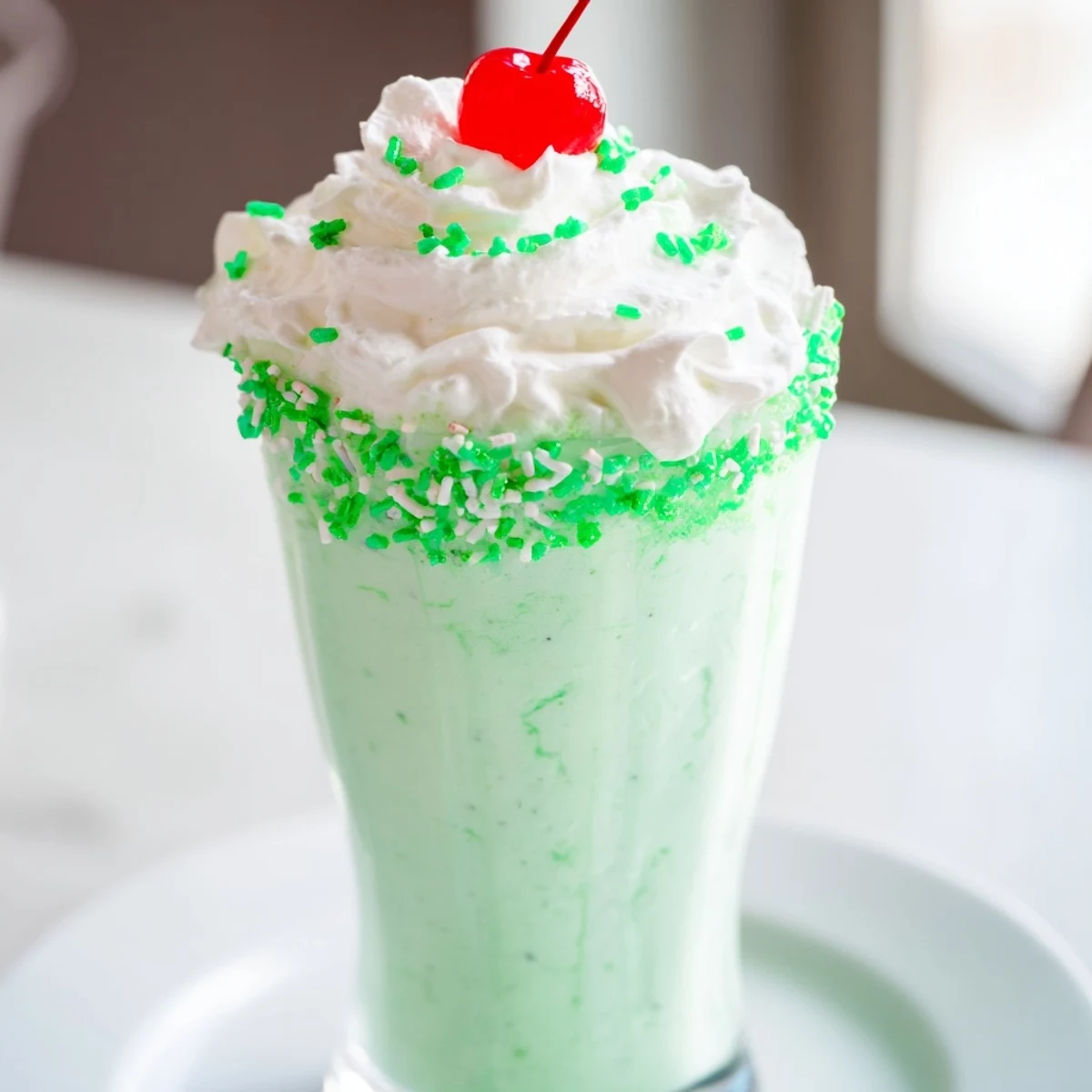 Close-up of a creamy green Homemade Copycat Shamrock Shake being poured from a blender into a tall glass.
