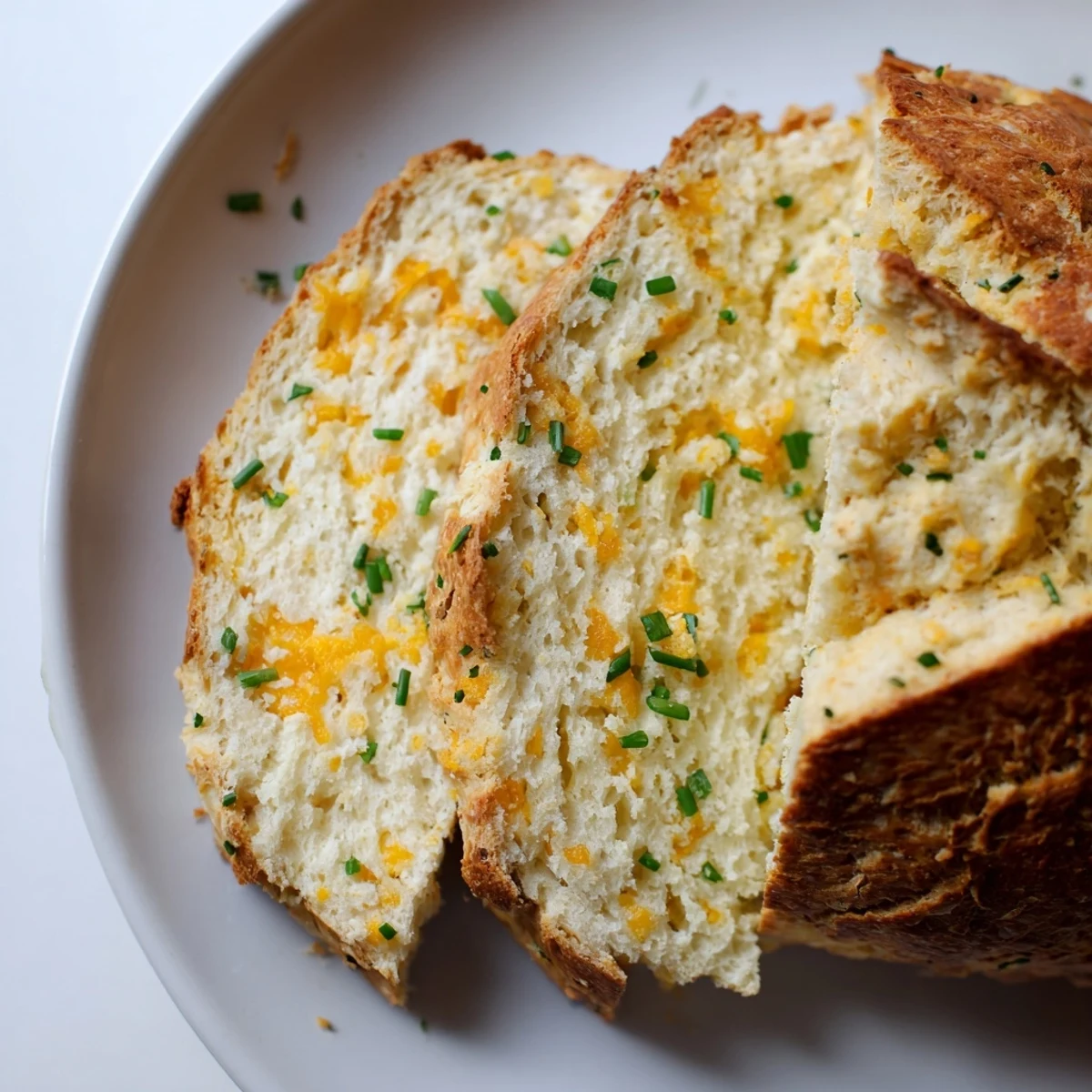 Freshly baked Savory Cheddar & Chive Irish Soda Bread loaf on a baking sheet, its deep X cut on top and aromatic herbs visible.