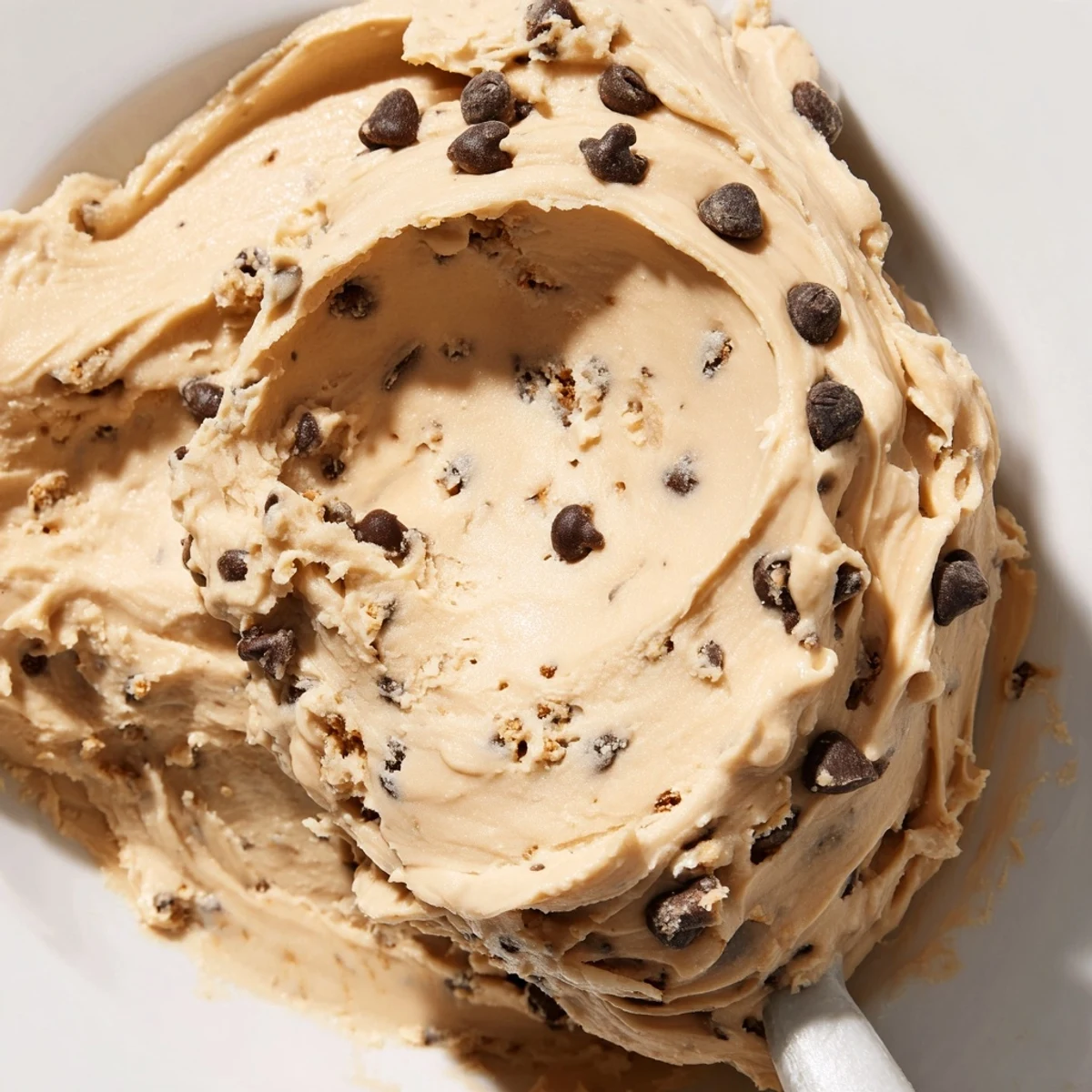 Creamy Cookie Dough Frosting with mini chocolate chips in a bowl beside a cupcake.
