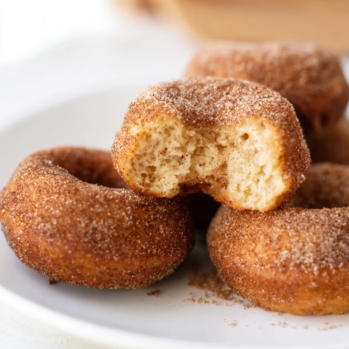 Warm Delicious Baked Cinnamon Sugar Donuts You Cant Resist arranged on a white plate next to a steaming mug of coffee.