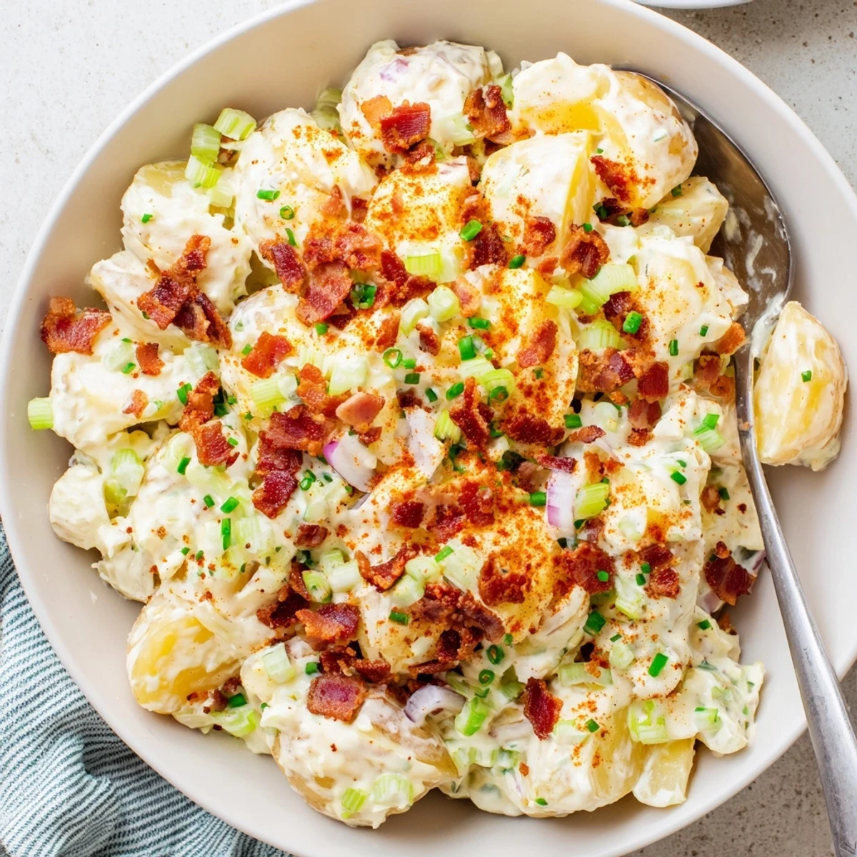 Classic American steakhouse side dish featuring creamy potato salad garnished with fresh chives and a sprinkle of paprika on top.