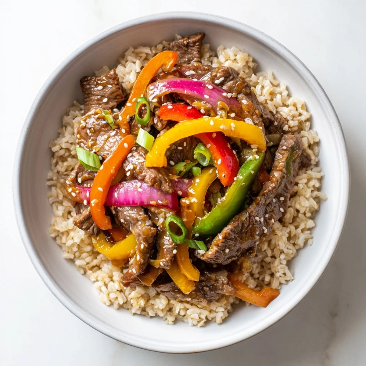 Served in a ceramic bowl over steamed brown rice, this Healthy Beef and Pepper Rice Bowl features vibrant red, yellow, and green peppers.
