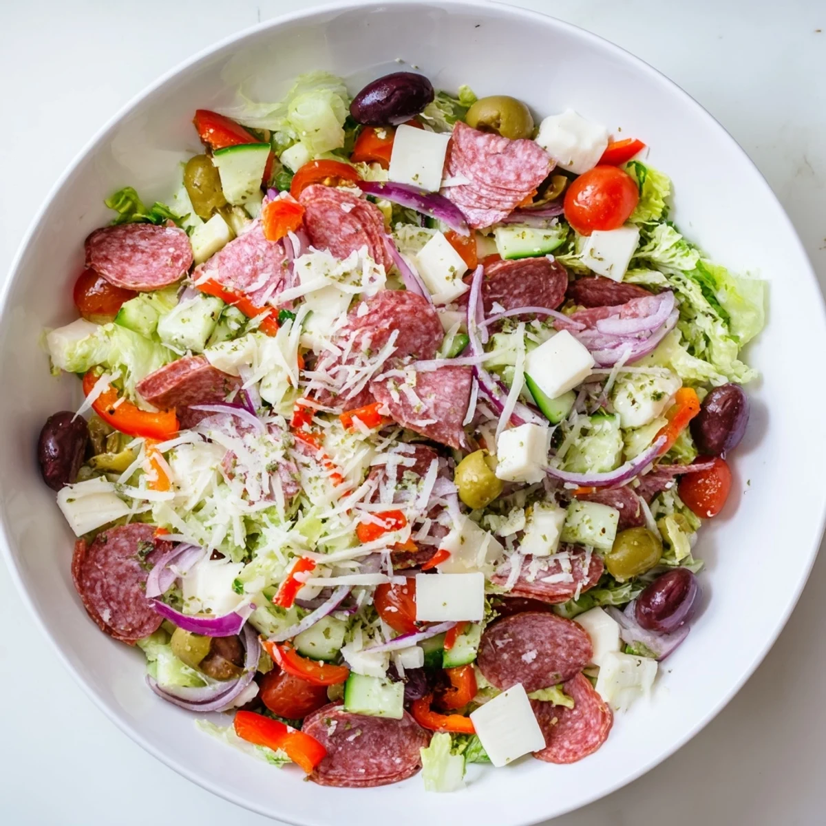 Fresh Italian chopped salad arranged on white plate featuring olives, cherry tomatoes, pepperoncini and zesty dressing