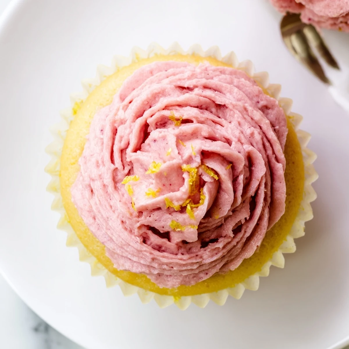 Fluffy lemon cupcakes with strawberry buttercream frosting piped into pink swirls on dessert table