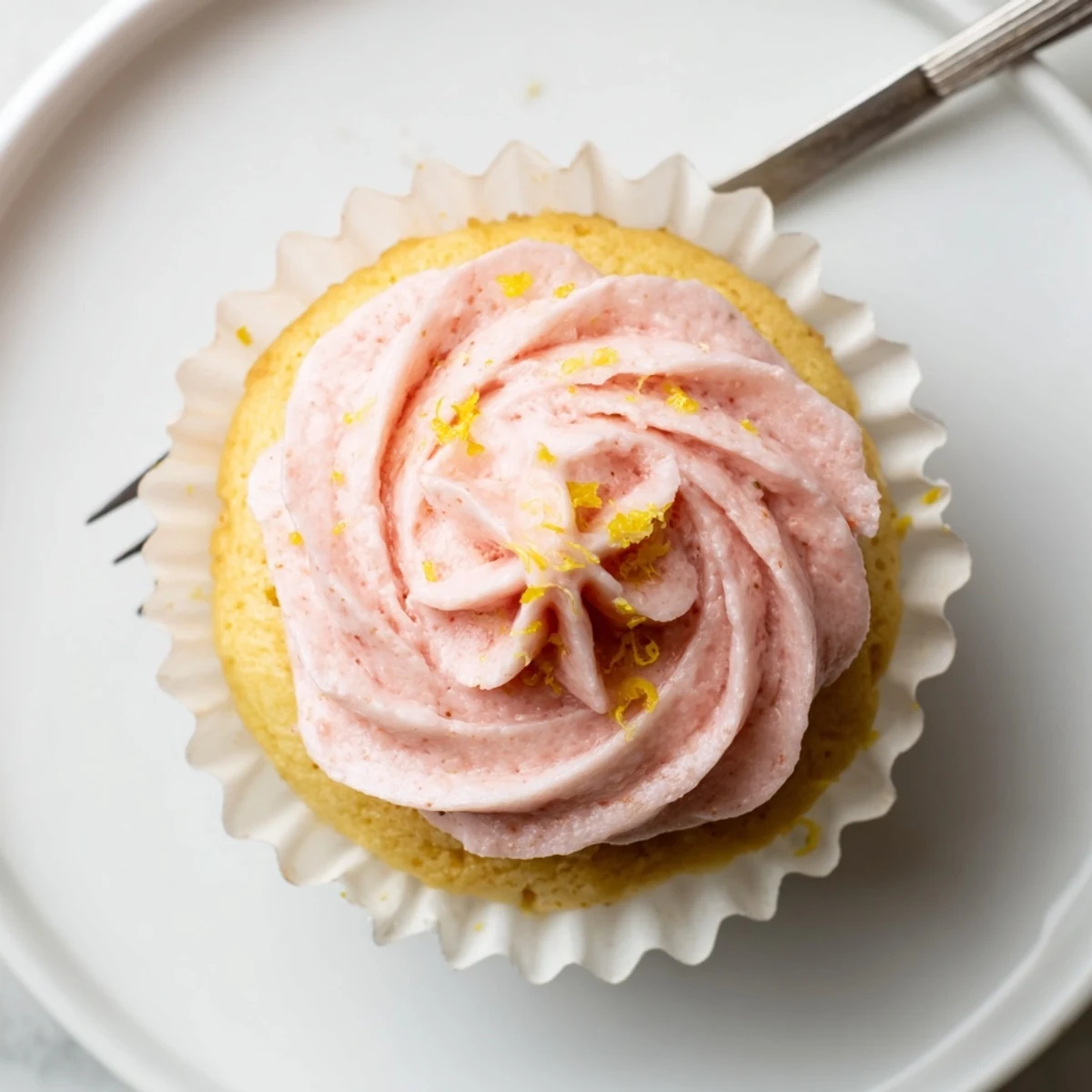 Homemade lemon cupcakes with strawberry buttercream decorated with lemon zest curls on wire rack