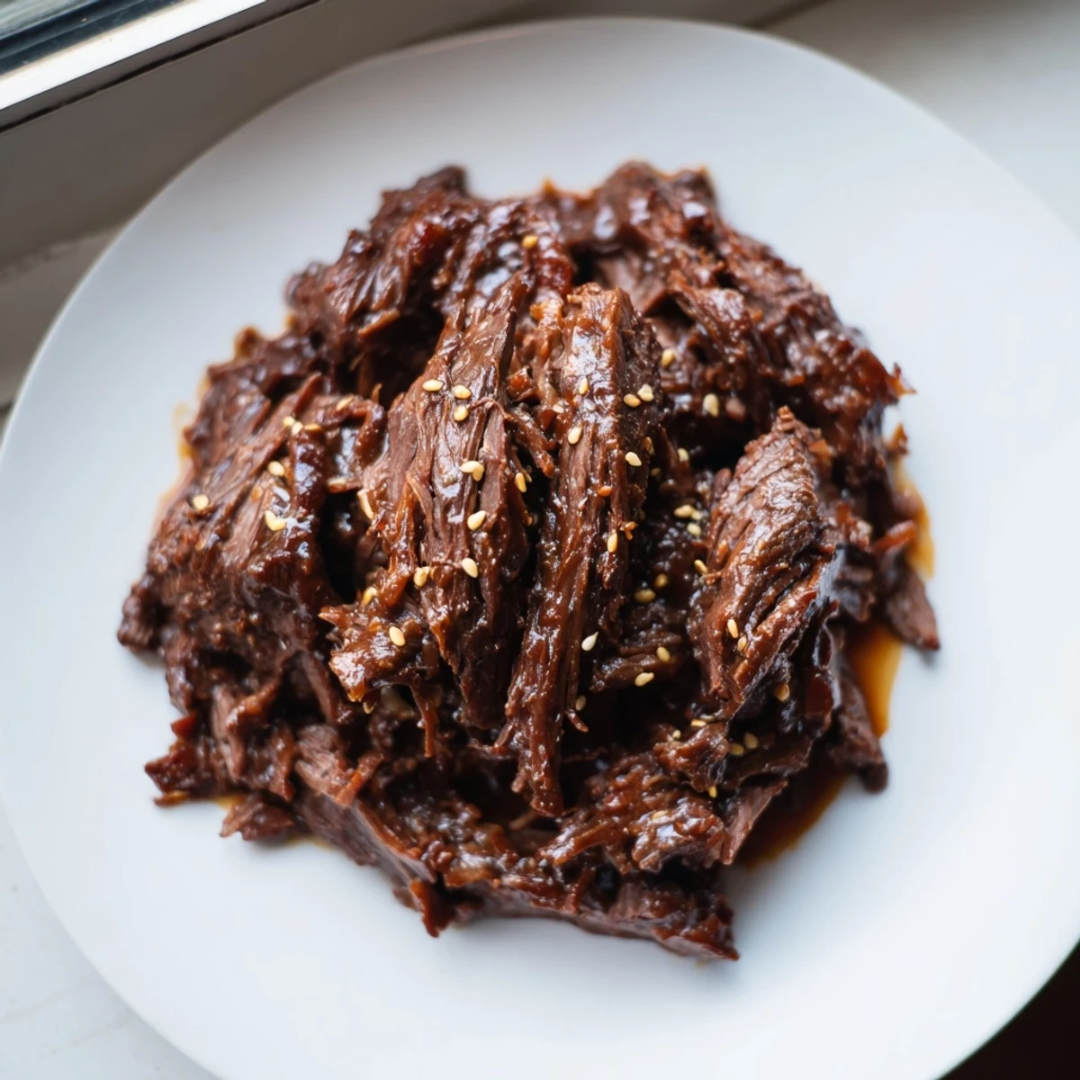 Slow cooker Korean beef with tender shredded pieces coated in glossy brown sauce and garnished with green onions.
