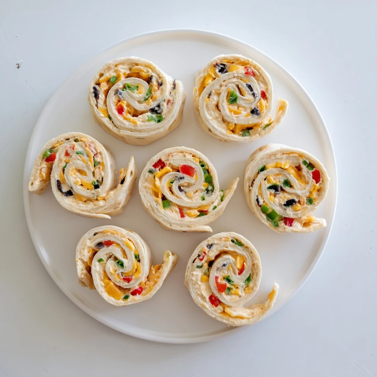 Colorful easy tortilla pinwheels filled with creamy cheese, peppers, and green onions on a white serving platter