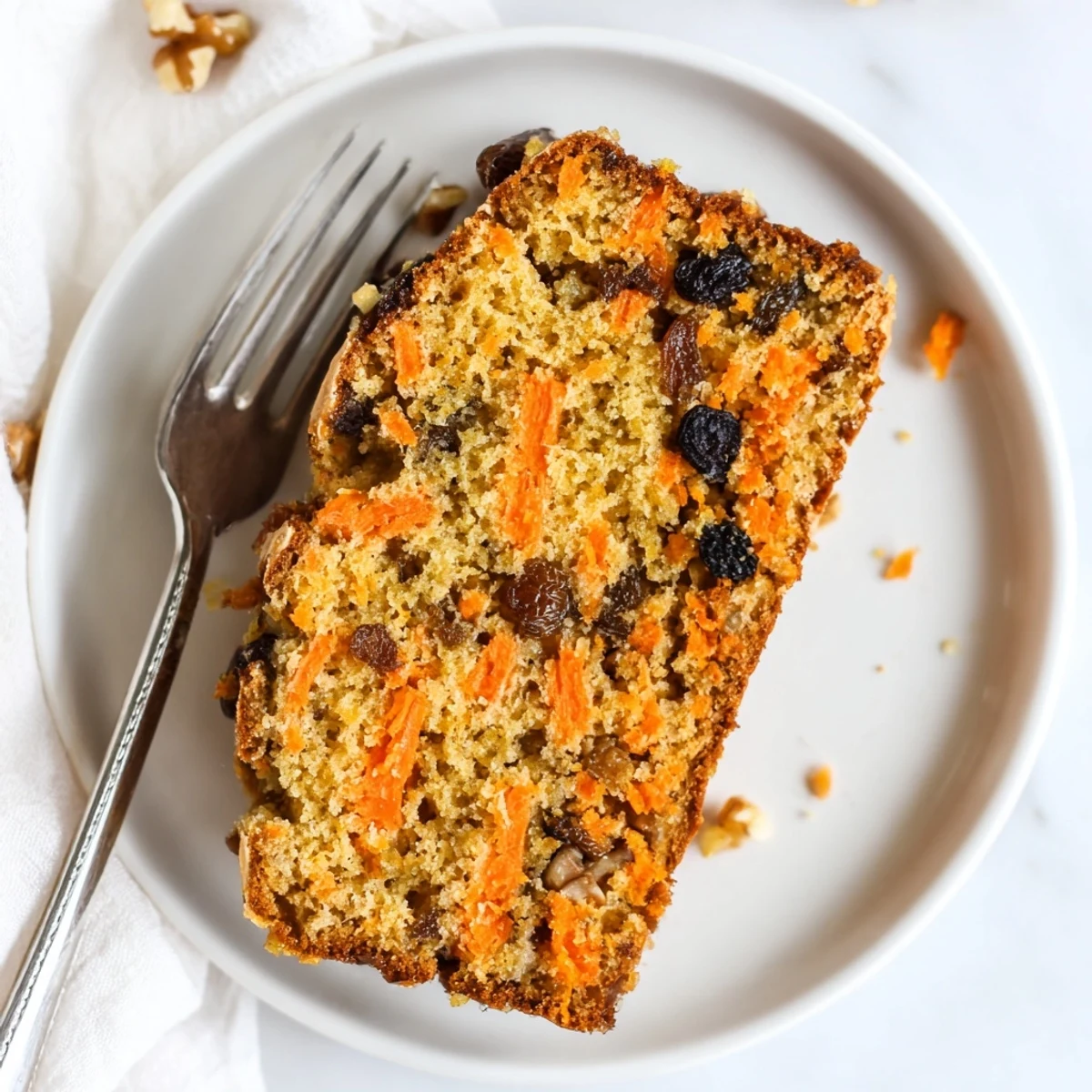Golden slice of Greek yogurt carrot cake topped with chopped walnuts on a rustic white serving plate