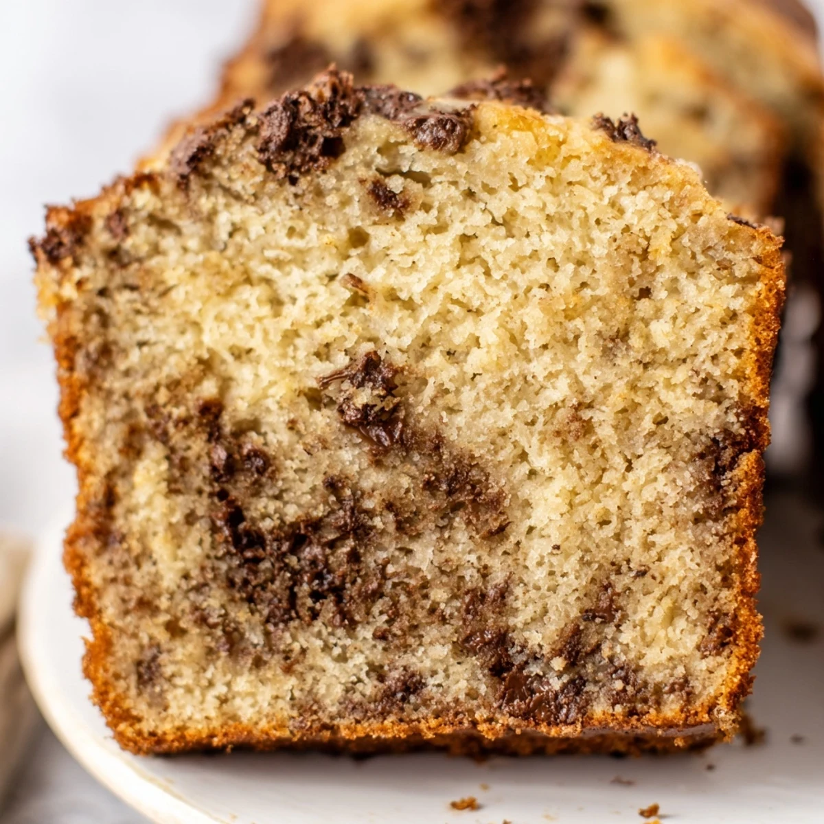 Slice of warm chocolate chip banana bread showing tender crumb and gooey chocolate chunks