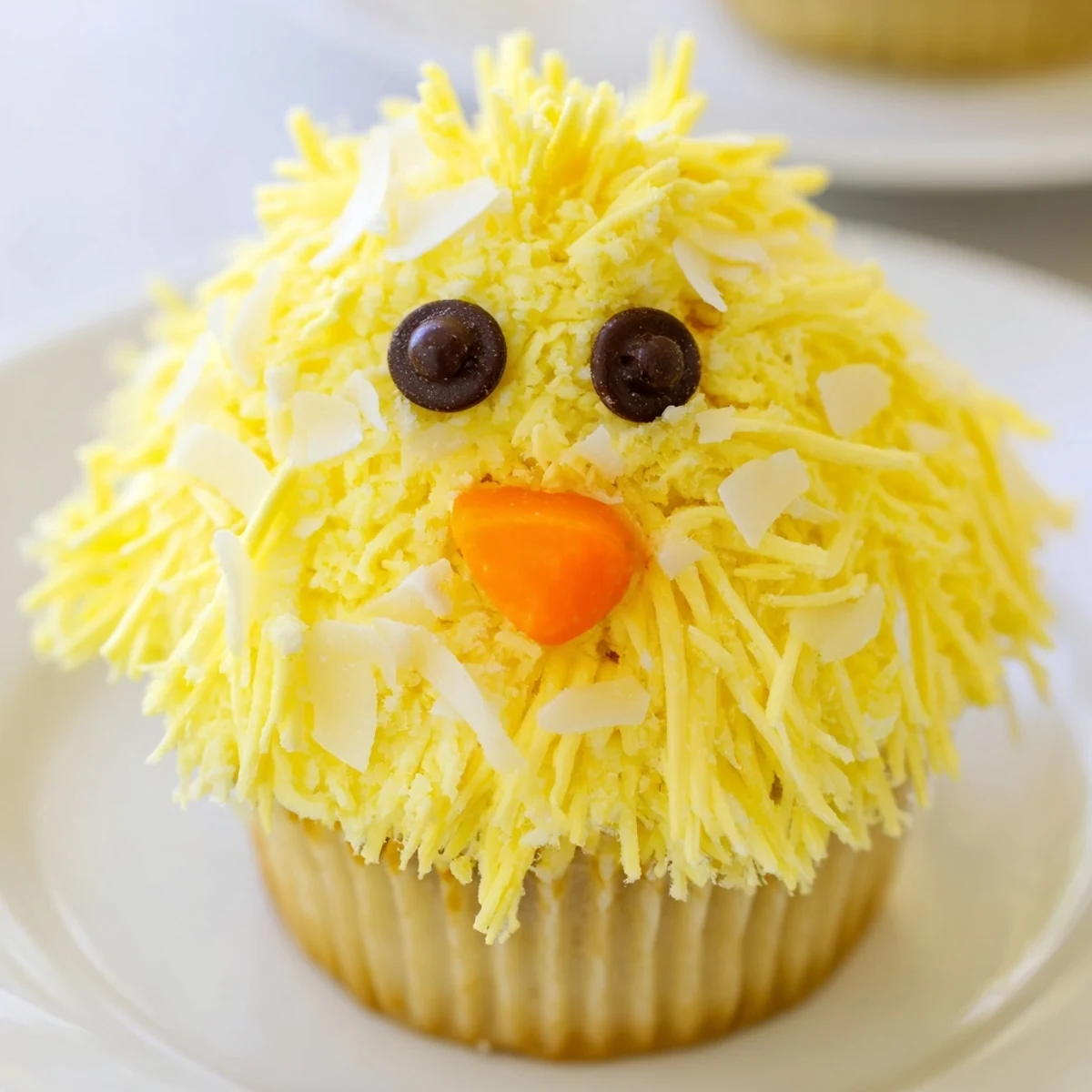 Decorated Easter Chick Cupcakes featuring chocolate chip eyes and orange candy beaks on pastel liner