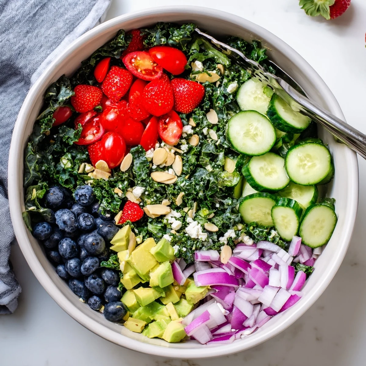 Colorful summer kale salad topped with feta, almonds, and fresh berries