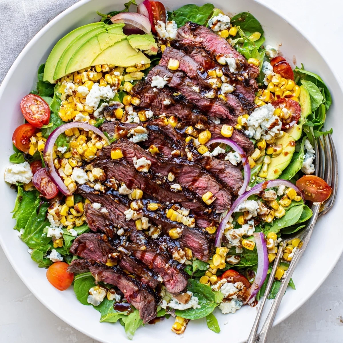 A generous platter of balsamic steak Gorgonzola salad drizzled with vinaigrette alongside ripe avocado and cherry tomatoes.