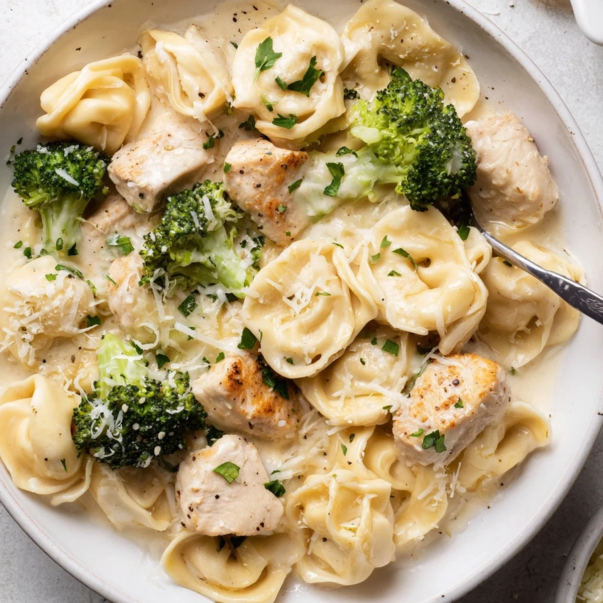 Steaming bowl of Creamy Garlic Parmesan Tortellini Chicken Broccoli Recipe, golden chicken