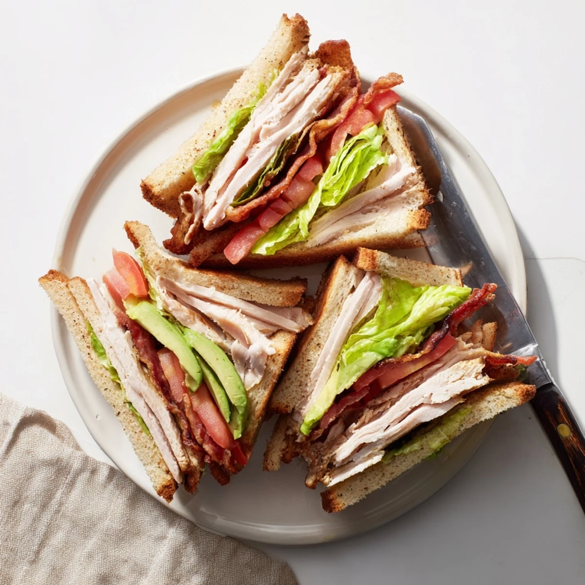 Diagonally cut California Club Sandwich revealing triple layers of turkey, bacon, ripe tomato and ripe avocado slices