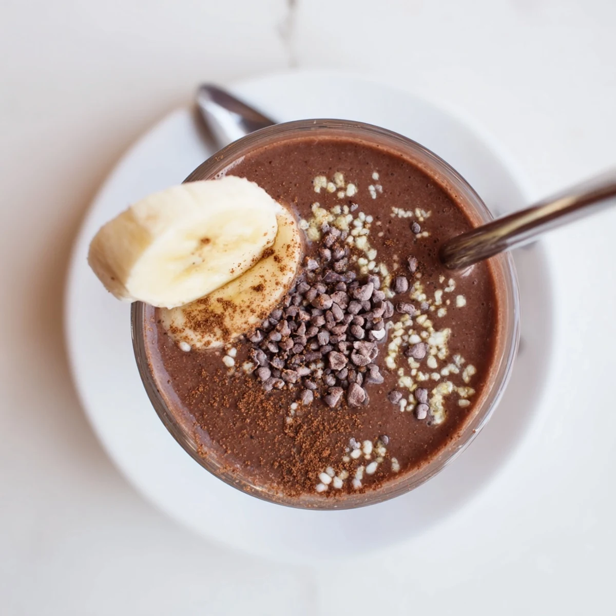 Thick glass filled with rich raw chocolate banana shake topped with cacao nibs
