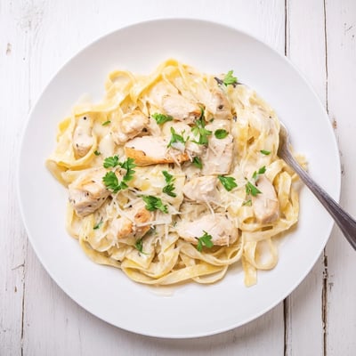 Golden chicken alfredo pasta tossed in velvety white sauce with grated Parmesan cheese and chopped green parsley.