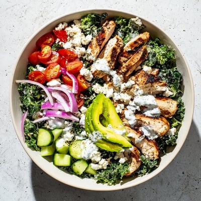 Juicy sliced chicken atop massaged kale with tomatoes, cucumber, and avocado in bowl