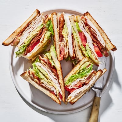 Golden toasted California Club Sandwich layers featuring roasted turkey, crispy bacon, creamy avocado and fresh vegetables