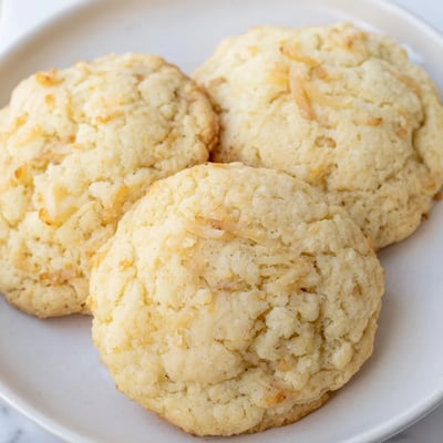Soft and buttery coconut cookies arranged on a white plate beside a steaming mug of tea